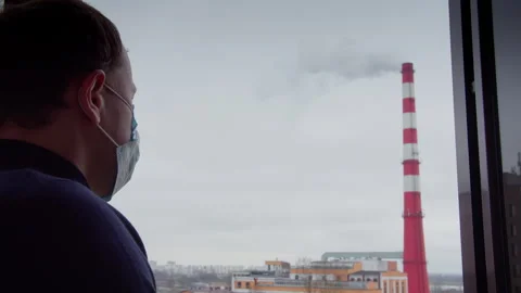 Man in protective mask looks through window at factory stack, air pollution Stock Footage 307757540