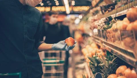 Man in a protective mask when selecting apples at the supermarket. Stock Photos