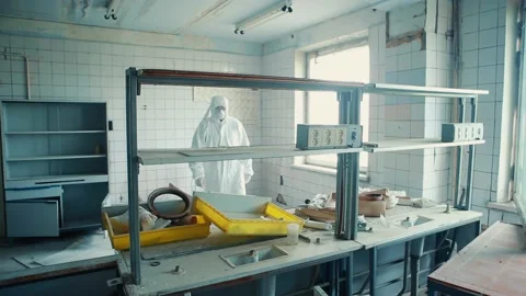 A man in a protective suit and goggles fits in a destroyed laboratory. Video stock 131439076