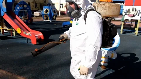 A man in a protective suit and mask disinfects a children's playground. Measures Stock Footage 127298513