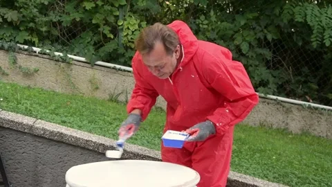 Man in protective suit applying white paint on wooden tabletop outdoors. Video stock 327654464