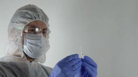 A man in a protective suit holds two ampoules in his hands 4K Vídeo Stock 126806811