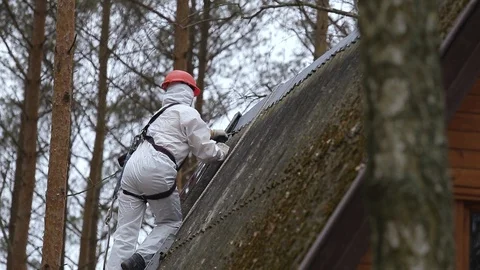 Man in a protective suit pries asbestos material off of a roof of a rural home Stock Footage 89739764