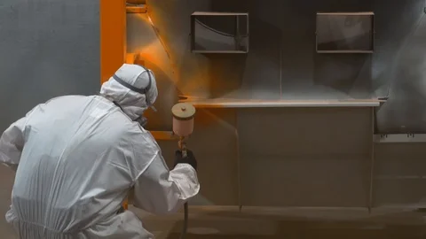 Man in protective suit squat down, spray gun in hand, paint metal body of boiler Stock Footage 120062369