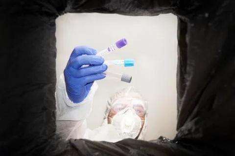 Man in a protective suit throws used medical test tubes into a trash can. Bot Stock Photos