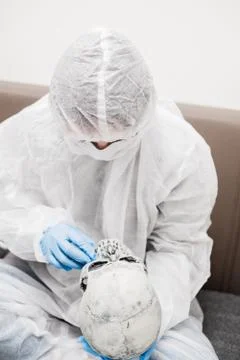 Man in protective white translucent suit, blue rubber gloves, medical mask sits Stock Photos