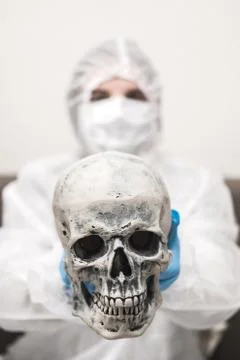 Man in protective white translucent suit, blue rubber gloves, medical mask sits Stock Photos