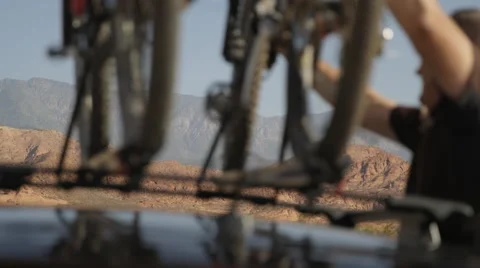 Man pulling bike off top rack of vehicle with scenic mountain background Stock Footage 57125315