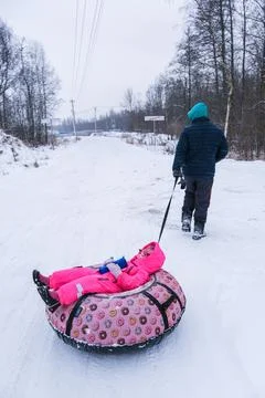 Man pulling a child on a pink snow tube in a snowy winter landscape. Fun winter Stock Photos