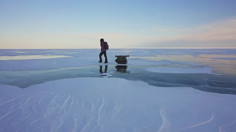 Man pulling equipped sledge over frozen ice. Hiking alone. Snowy severe scenery Stock Footage 165702505