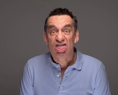 Man pulling face sticking out tongue on grey background Foto stock