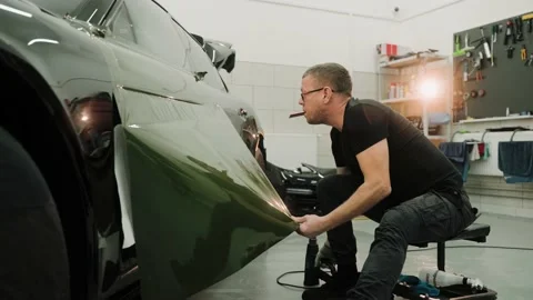 Man pulling the film down while vinyl wrapping a car in a work garage, 스톡 동영상 171959106