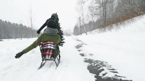 Man pulling girl on a sled at snow. Winter fun Stock Footage 99508965