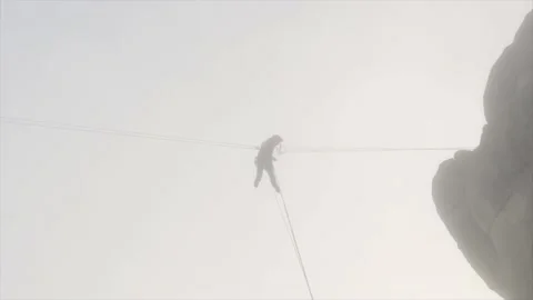 Man pulling himself to a rock on a zip line through a thick fog. Emergency Video stock 149727890