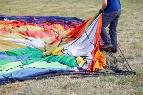 A man is pulling a large colorful parachute out of the grass Stock Photos