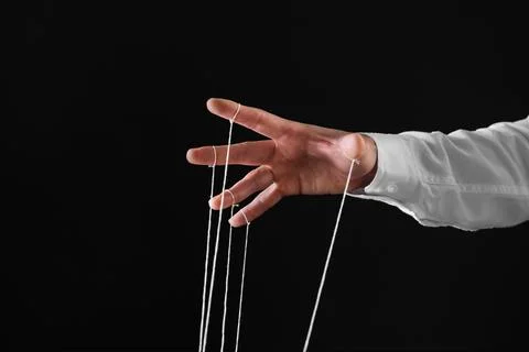 Man pulling strings of puppet on black background, closeup. Space for text Stock Photos