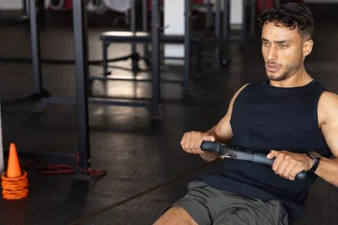Man pulling V-bar cable row handle while sitting on bench at gym weight room, Stock Photos