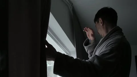 A man pulls back the curtains on the window Видео 332013140