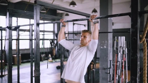 Man pulls up on bar in gym, wears lift and grip gear and white t-shirt Stock Footage 117043173