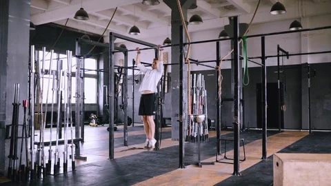 Man pulls up on bar in gym, wears lift and grip gear and white t-shirt Stock Footage 117371312