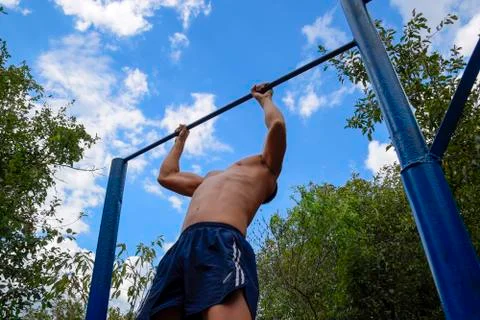 The man pulls himself up on the bar. Playing sports in the fresh air. Horizon Stock Photos