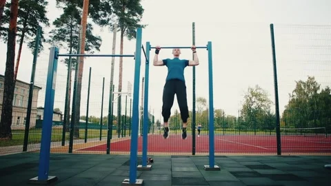 A man pulls himself up on a horizontal bar, exercising on an open sports ground. Stock Footage 149754722