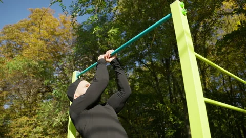 A man pulls himself up on a horizontal bar on a sports field Stock Footage 221568649