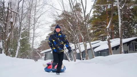 Man pulls inflatable sled with daughter by resort cottages Stockbeeldmateriaal 138884890
