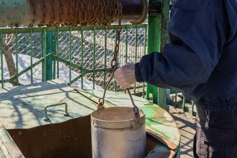 A man pulls a metal bucket from a weathered water well using a rustic chain Stock Photos