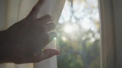Man pulls open window curtain or drape to reveal sunny day outdoors as sun Stock Footage 323430819