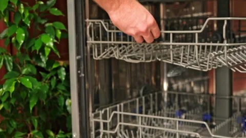 The man pulls out the dishwasher basket and unloads clean glasses, cups, bowls Stock Footage 244638026