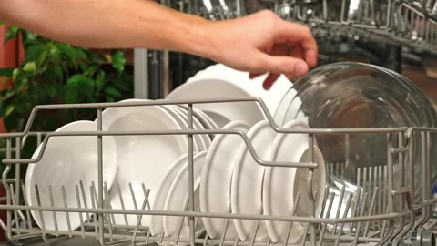 Man pulls out dishwasher basket and unloads clean plates. Release of dishwasher Stock Footage 244804092