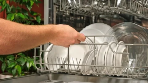 Man pulls out dishwasher basket and unloads clean plates. Release of dishwasher Stock Footage 244804251