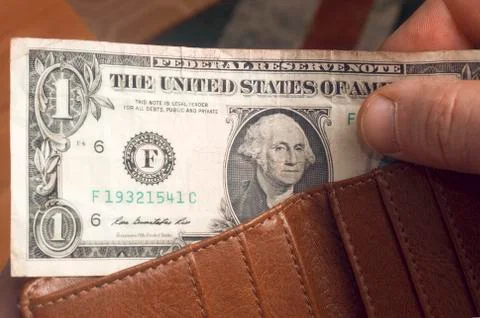 Man pulls out a dollar bill from a brown leather wallet Stock Photos