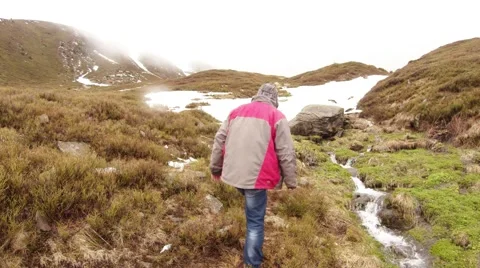 Man Pulls Out Object From Water Near Mountain Stream on the Mountain Video stock 63961314