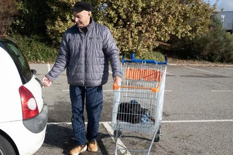 Man pulls shopping cart while heading to his car in parking area Stock Photos