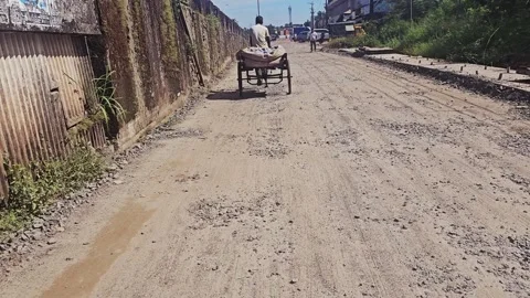 A man pulls a simple wooden cart along a very rough, unpaved, dusty road in what Video stock 320796809