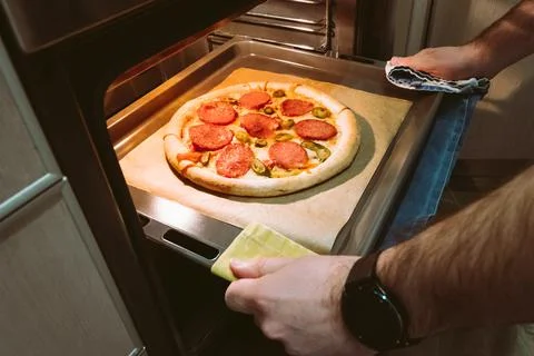 A man pulls a tray of pepperoni pizza from the oven at home Stock Photos