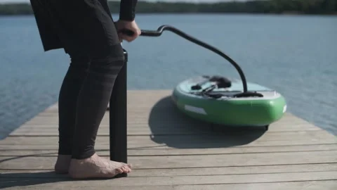 Man pumping stand up paddle board standing on wooden bridge on lake shore. SUP Stock-Footage 243428354