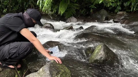 Man Purifying River Water with Filter in Lush Forest, Medium Shot Stock Footage 324502256