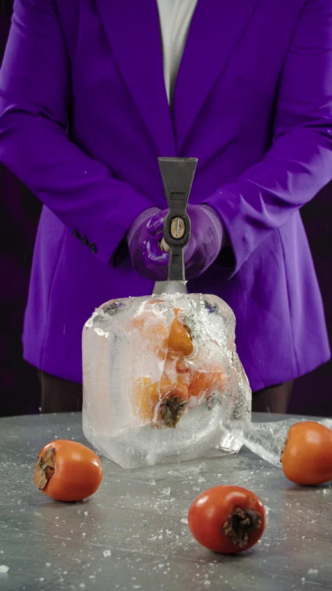 A man in a purple jacket breaks a large piece of ice with a hammer Stock Footage 302882070