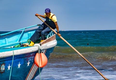 Man pushes against sand to release boat from the surf in Puerto Lopez, Ecuado Foto stock
