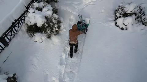 Man pushes battery-powered snow blower along narrow path covered with white snow Stock-Footage 326967192