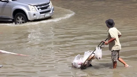 A man pushes a cart with full plastic bags on a flooded street, slow motion Stock Footage 220825009