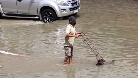 A man pushes a empty cart on a flooded street Stock Footage 234459768