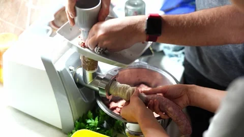 Man pushes meat into a meat grinder, and a woman fills the intestines with Stock Footage 266854232