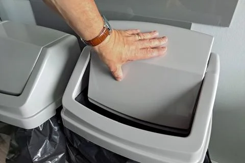Man pushes open grey plastic flip top lid on kitchen waste bin with open hand Stock Photos
