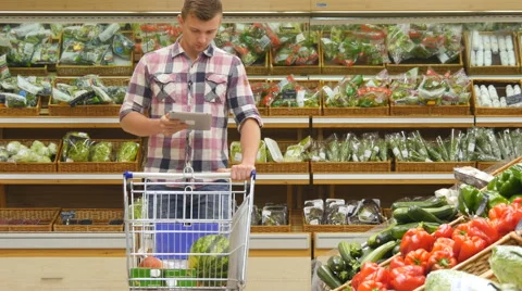 Man pushing cart along the grocery aisles at store and using tablet pc Stock Footage