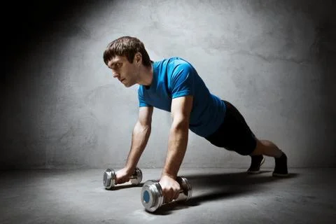 Man pushing up from the dumbbells on wall backdrop Stock Photos