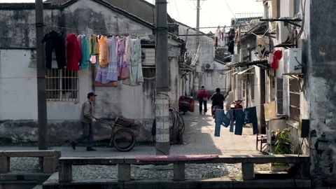 Man pushing a handcart down historic Chinese alleyway lined with drying laundry Stock Footage 341075784